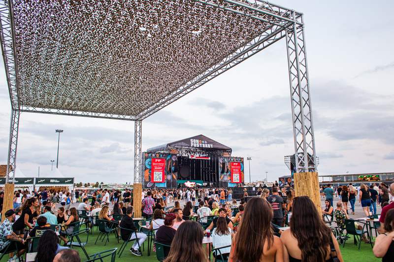 La explanada de día con las mesas llenas y el escenario al fondo