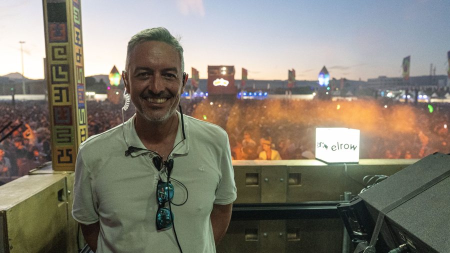 Un técnico de producción sonríe en lo alto del escenario con el recinto lleno detrás